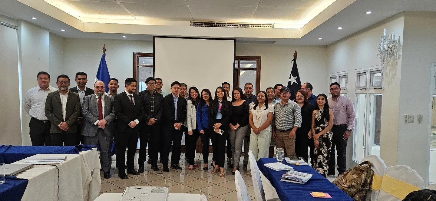 Fotografía grupal de una treintena de participantes de la capacitación en una sala de reuniones, entre las banderas de Honduras y de Chile.