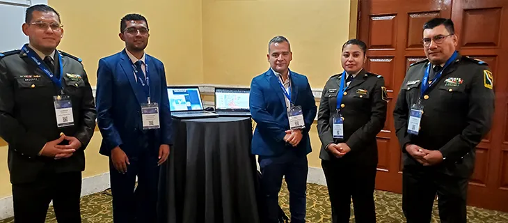 Cinco personas posan junto a una mesa con dos portátiles que muestran visores cartográficos; tres de ellas visten uniforme institucional.