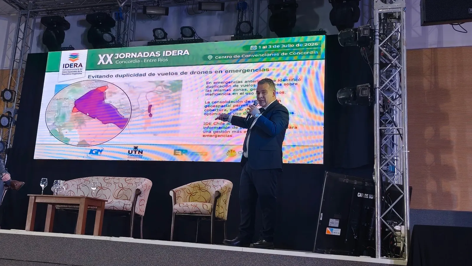 Un expositor presenta en las XX Jornadas IDERA la ponencia «Evitando duplicidad de vuelos de drones en emergencias», ante una diapositiva con el mapa de las zonas sobrevoladas.