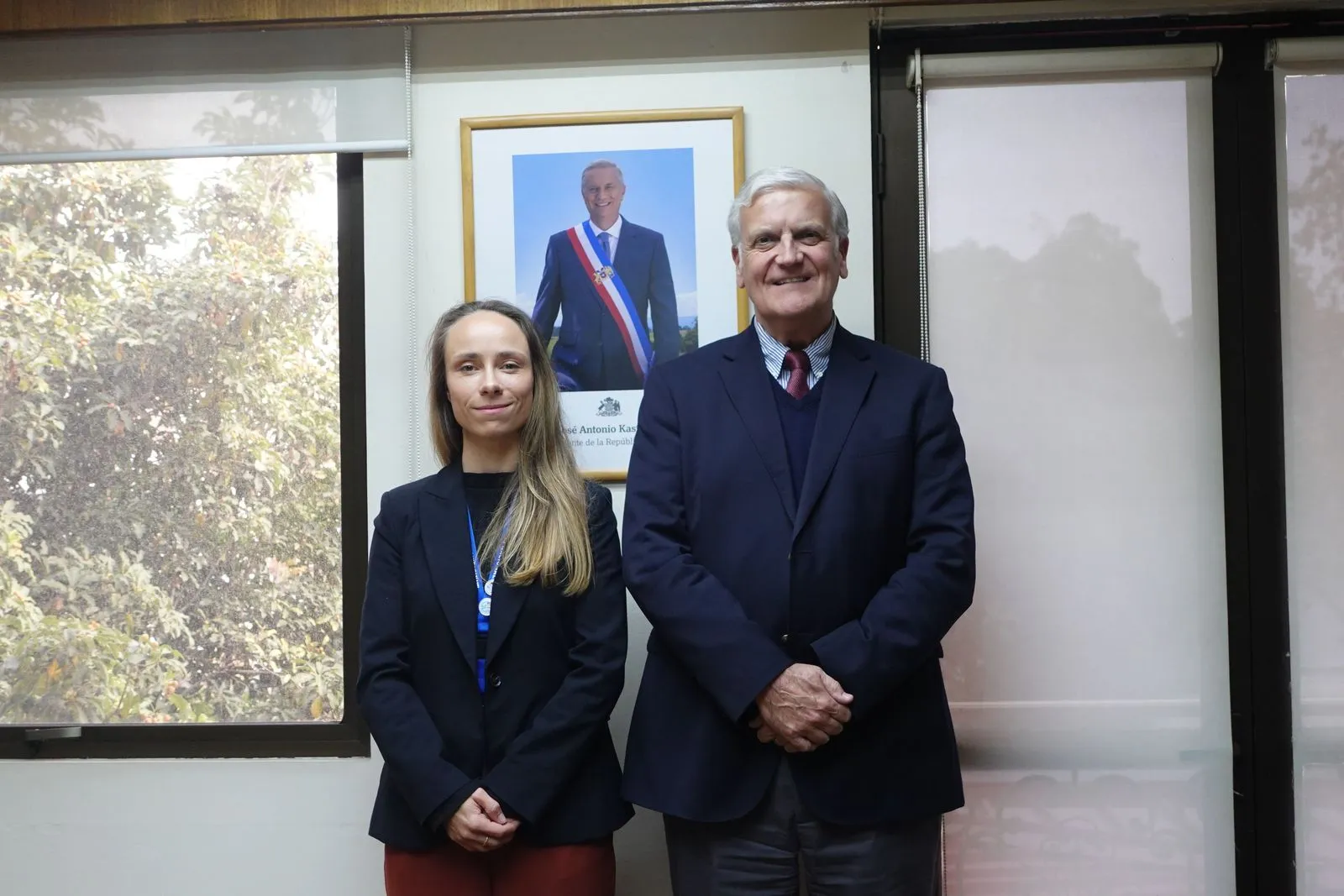 Dos personas posan de pie ante el retrato oficial del Presidente de la República, en una oficina institucional.