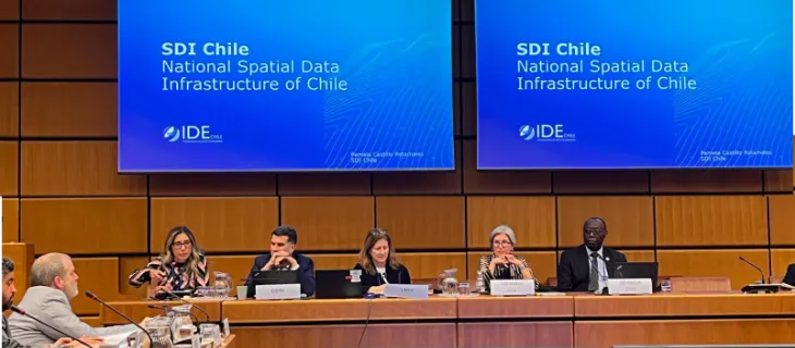 La mesa de panelistas durante la presentación «SDI Chile — National Spatial Data Infrastructure of Chile», proyectada en las dos pantallas de la sala.