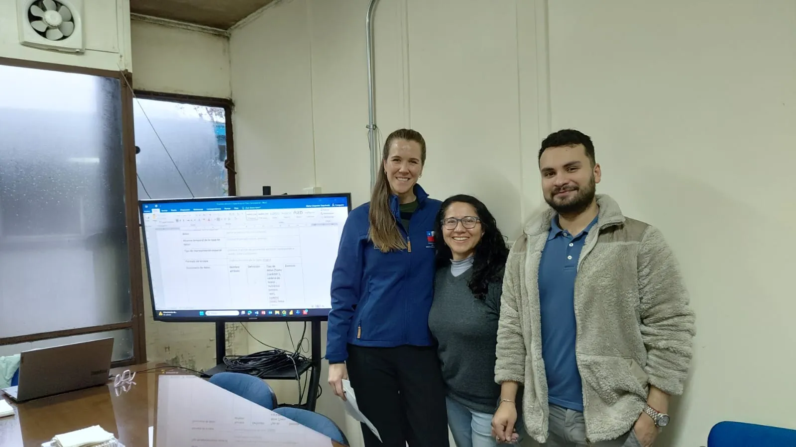 Tres profesionales ante una pantalla con una plantilla de especificación de datos geoespaciales, en la capacitación de la Región de Los Lagos.