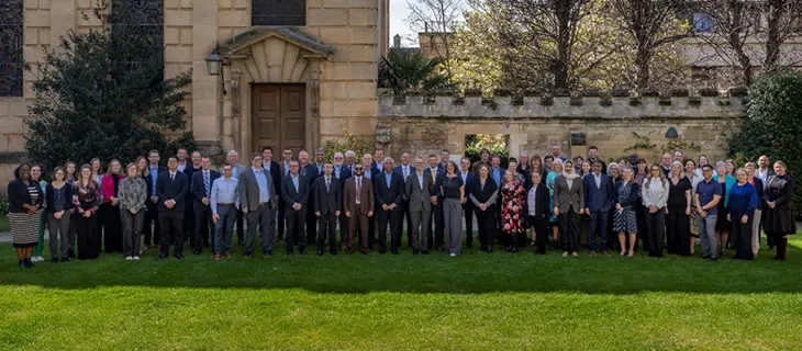 Fotografía grupal de los asistentes a la conferencia sobre el césped, ante un edificio de piedra de Cambridge.