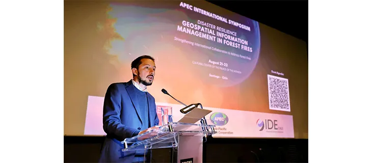 Un expositor habla desde el atril ante la pantalla de apertura del simposio internacional APEC sobre gestión de información geoespacial en incendios forestales.