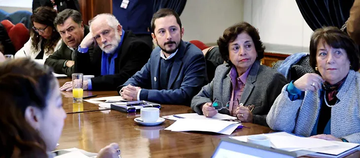 Varias personas siguen la sesión sentadas a una mesa de reuniones.