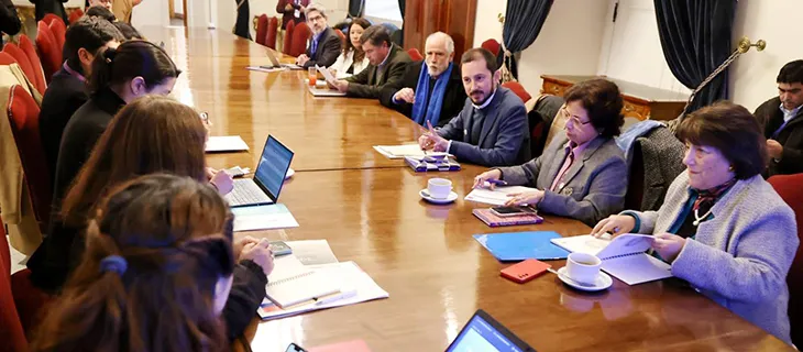 Vista general de la sala, con los asistentes a ambos lados de una larga mesa de madera.